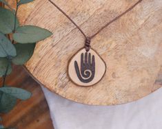 A handmade boho necklace with an engraved hand made from local hardwood. Since I make each piece of jewelry by hand and each piece of wood is unique, your delivered necklace may vary slightly from the product images. I hand burn the design into the wood and treat it with natural oil. The oil protects the pendant from external influences and keeps it looking beautiful for a long time. Nevertheless, the chain should be removed before showering or swimming. The pendant is attached to a waxed cotton cord with adjustable length. So the length of the necklace can be varied. The pendant has a diameter of about 3 cm. Each piece of my shop is from fallen tree limb, so no trees are ever damaged.  Visit my shop to find more hippie and festival jewelry! Vegan product. Handmade with love. Plastic-free Wood Burned Necklace, Adjustable Artisan Natural Wood Necklace, Adjustable Natural Wood Pendant Jewelry, Bohemian Wood Necklaces Perfect For Gifts, Handmade Wooden Jewelry For Meditation, Bohemian Wood Necklace For Gift, Bohemian Wood Necklace As Gift, Bohemian Wood Necklace Perfect As A Gift, Handmade Natural Wood Pendant Jewelry