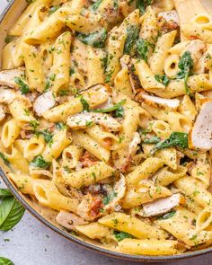 a skillet filled with pasta, chicken and spinach on top of a table