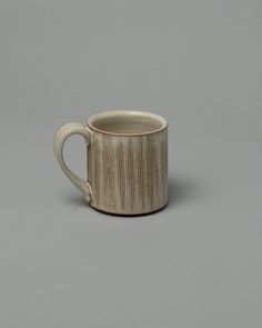 a white and brown coffee cup sitting on top of a table next to a gray wall