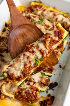 a wooden spoon scooping some food out of a casserole dish with zucchini