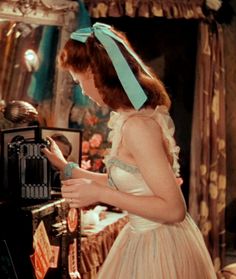 a woman in a pink dress looking at an old fashioned typewriter with a blue bow on her head