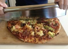 a person cutting up a pizza on top of a wooden board with a metal spatula