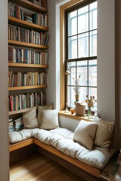 a window seat in front of a bookshelf filled with lots of books and pillows