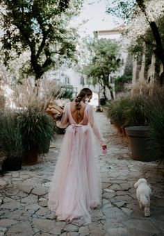 a woman in a long pink dress walking down a path with a white dog behind her