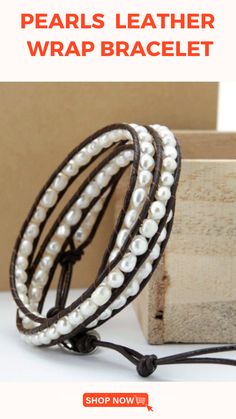 the leather wrap bracelet has pearls on it and is next to a box with a wooden block