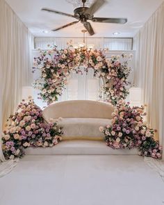 a white couch sitting under a ceiling fan next to a flower covered wall with flowers on it