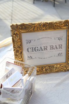 an ornate gold framed sign sitting on top of a white table cloth covered tablecloth