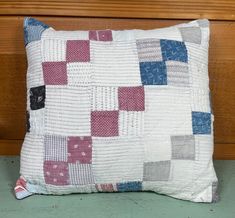 a white pillow with red, blue and grey squares on it sitting next to a wood paneled wall