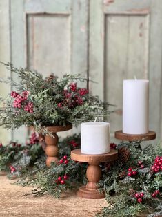 three candles sitting on top of a wooden table covered in greenery and berries with pine cones