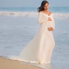 a pregnant woman standing on the beach with her arms around her waist, wearing a white dress