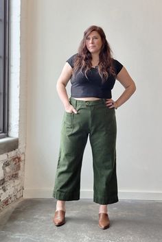 a woman is standing in front of a window wearing green pants and a black shirt