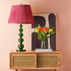 a vase with flowers on top of a table next to a lamp and a painting