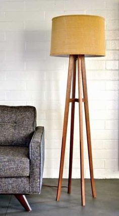 a wooden floor lamp next to a chair in a room with white bricks on the wall