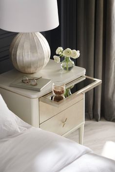 a white lamp sitting on top of a wooden table next to a night stand with flowers