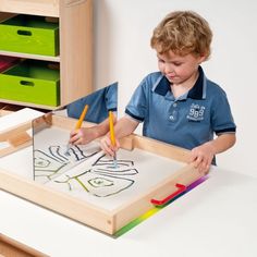 a little boy that is sitting at a table with some crayons in front of him