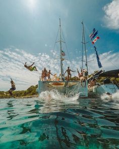 a group of people jumping off the back of a boat into the ocean while another person swims in the water