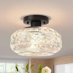 a light that is hanging from the ceiling above a table with flowers and vases on it