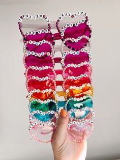 a hand holding up several pairs of sunglasses with beads and pearls on the sides, all in different colors