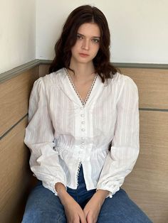 a woman sitting on top of a wooden bench wearing a white shirt and blue jeans