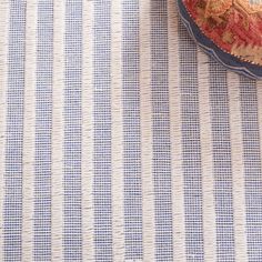 a blue and white striped table cloth with a red flower on it next to a bowl