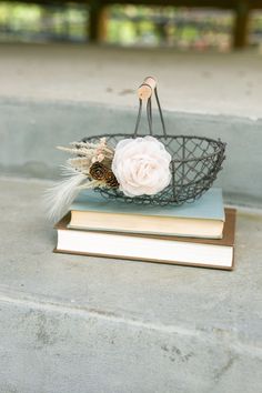 a basket with flowers and feathers on top of two books sitting on the ground next to each other