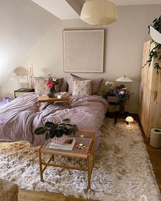 a bedroom with a bed, nightstands and plants on the table in front of it