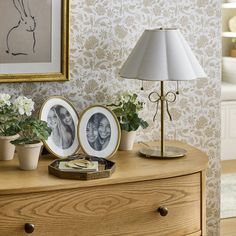 a dresser with two pictures on it and flowers in vases next to the drawers