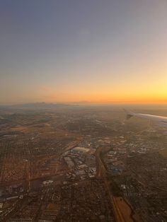 an airplane wing flying over a city at sunset