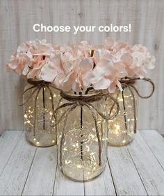 three mason jars filled with pink flowers and string lights