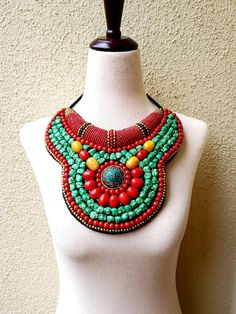 "Striking Tibetan turquoise and coral bib collar necklace in faux teal green turquoise, coral and amber beads, with a stunning central brass medallion. Perfect with a flowing caftan or an itsy black bikini. Perfect anywhere you are barefoot! Wear your hair up, with a bright ribbon or turban, or wear it down! You don't need much else! Eye-catching geometric pattern with a mix of smooth and textured beads. This is a handmade reproduction of a Tibetan tribal neck piece or Skeypuk, which is worn as Bohemian Turquoise Bib Necklace With Colorful Beads, Red Beaded Bohemian Bib Necklaces, Red Bohemian Bib Necklace For Festivals, Bohemian Red Bib Necklace With Round Beads, Green Bohemian Beaded Necklaces, Bohemian Bib Necklace With Colorful Beads, Handmade Turquoise Bohemian Bib Necklace, Green Turquoise Necklace With Colorful Beads For Festivals, Multicolor Bohemian Turquoise Necklace For Festivals