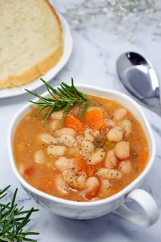 a white bowl filled with beans and carrots next to a slice of bread on top of a table