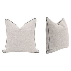 two grey pillows with black piping on the sides and one white pillow in the middle