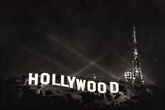 the hollywood sign lit up at night with lights in the sky and buildings behind it