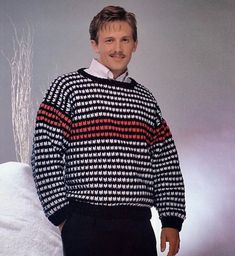 a man standing in front of a white couch wearing a black and red striped sweater