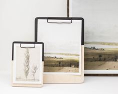 two framed pictures are sitting next to each other on a table with a clipboard in front of them