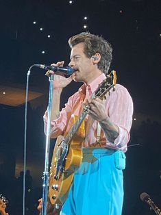 a man singing into a microphone while holding a guitar in his right hand and wearing blue pants