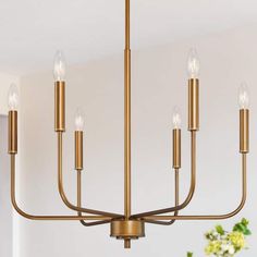 a brass chandelier with six candles hanging from the ceiling in a dining room