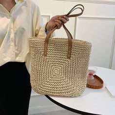 a woman holding a straw bag on her left hand while standing next to a white table