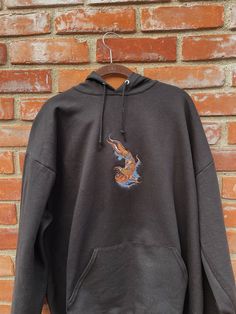 "Koi Fish Embroidered Hoodie -Embroidered on a cotton/polyester blend hoodie, this design is simple and minimalistic, perfect for every outfit! -Embroidery design measures 6\" x 3\" -See product pictures for shirt sizing chart. -Hanes/Gildan Brand depending on availability. -All sweatshirts are handmade on an embroidery machine so there may be slight differences, but we only sell the shirts that meet our high-quality standards. -To maintain the quality of your shirt and the embroidery design mak Embroidered Hoodie For Fall Streetwear, Black Embroidered Hooded Hoodie, Embroidered Black Hoodie For Fall, Embroidered Long Sleeve Hoodie For Streetwear, Black Hooded Embroidered Sweatshirt, Black Embroidered Hooded Sweatshirt, Black Embroidered Hoodie For Fall, Black Embroidered Long Sleeve Hoodie, Embroidered Black Hoodie For Streetwear