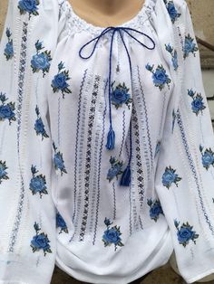 a woman wearing a white blouse with blue flowers and tassels on the neck