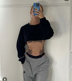 a woman taking a selfie with her cell phone while wearing sweatpants and sneakers