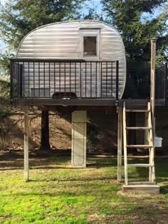 a metal structure with a ladder to the top and a small window above it, in front of trees