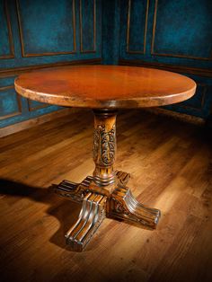 an old fashioned wooden table with ornate carvings on the legs and base, against a blue painted wall