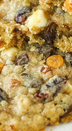 a cookie with raisins and other toppings sitting on a white plate next to a fork