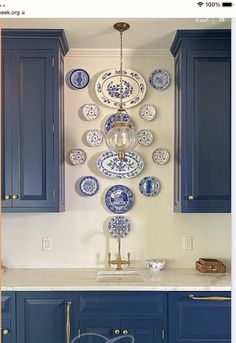 a kitchen with blue cabinets and plates hanging on the wall above the sink, in front of an overhead chandelier