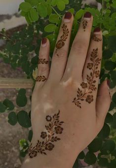 a woman's hand with henna tattoos on her left hand and green leaves in the background