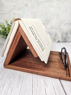 an open book sitting on top of a wooden stand next to glasses and a plant