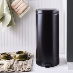 a black trash can sitting next to a towel rack and bowl on a rug in front of it