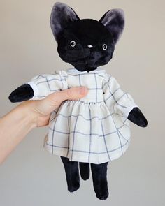 a hand holding a black and white stuffed animal with a dress on it's body