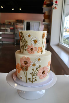 a three tiered cake decorated with flowers on a table in front of a window